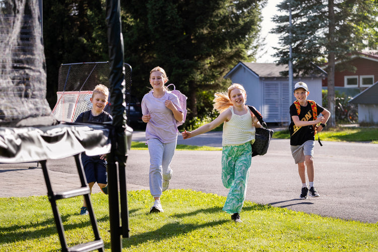 Four children running towards a trampoline on a sunny day.